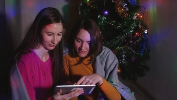 Sekme ile Noel ağacının yanında oturan genç kadın çift — Stok video