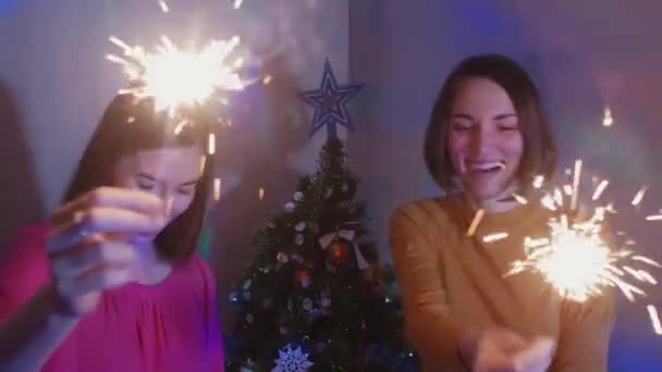 Two happy girls wih sparkler near a Christmas tree — Stock video