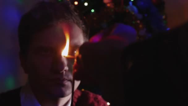 Jonge man bedrijf sparkler zitten in de buurt van een kerstboom — Stockvideo