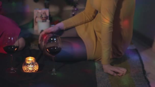 Jonge vrouwelijke paar zitten in de buurt van de kerstboom met glazen wijn met plezier — Stockvideo