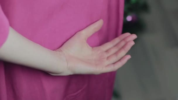 Hände eines Mädchens, das ein Geschenk hinter seinem Rücken in der Nähe des Weihnachtsbaums in Nahaufnahme hält — Stockvideo