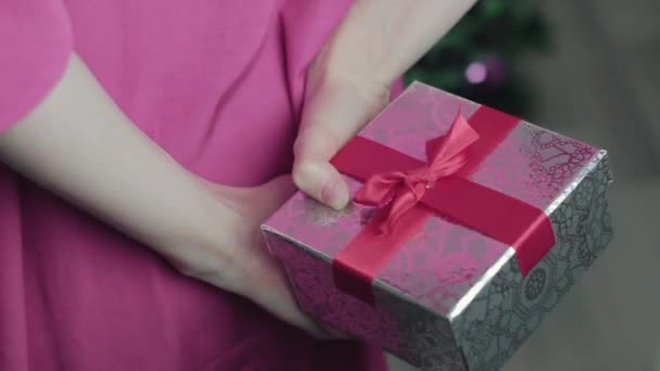 Hands of girl holding a gift behind his back near christmas tree close up — Stock video