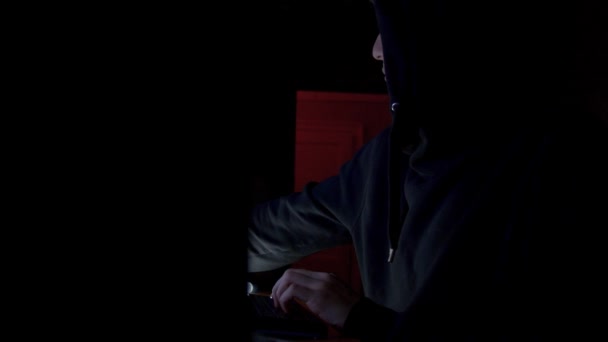 Хакер в капюшоне взламывает код с помощью компьютеров в темной комнате — стоковое видео