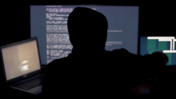 Хакер в капоті зламує код за допомогою комп'ютерів у темній кімнаті — стокове відео