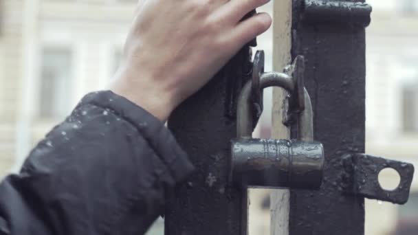 Cerca de la mano del joven que de pie y esperando cerca de puertas de hierro bajo la lluvia — Vídeo de stock