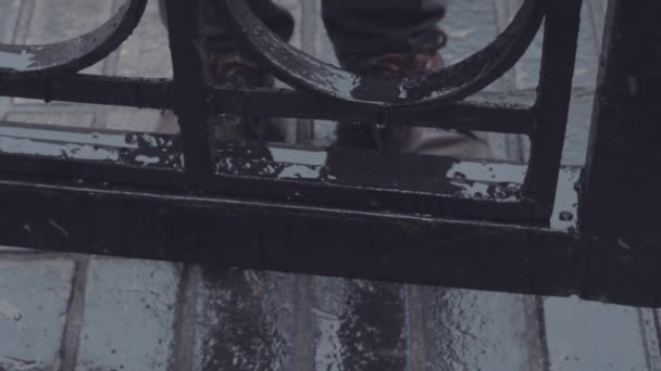 Gros plan pieds dans les chaussures de jeune homme qui se tient près des portes de fer sous la pluie — Video