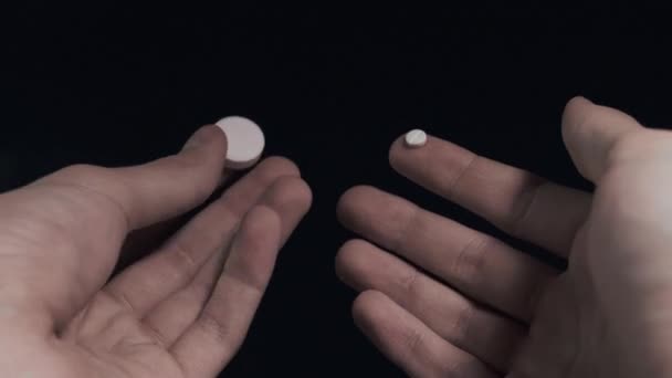 Man onderzoekt kleine pil en grote pil op handen close-up shot zwarte achtergrond Pov — Stockvideo