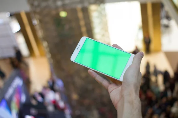 Male hands using smartphone with green screen in shopping mall. Lot of people at the background