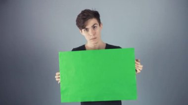 Siyah tişörtlü yeşil anahtar sayfa poster gri arka planı holding neşeli genç adam