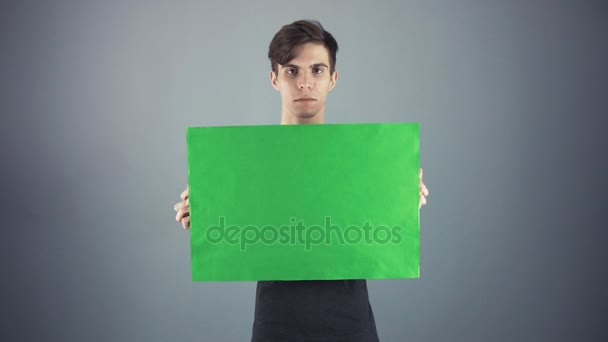 Znudzony młody mężczyzna w czarnej koszuli przytrzymując zielony klucz arkusz plakat szary tło — Wideo stockowe
