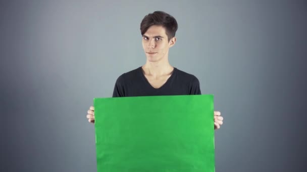 Flirting Молодой человек в черной рубашке держа зеленый ключ лист плакат серый фон — стоковое видео