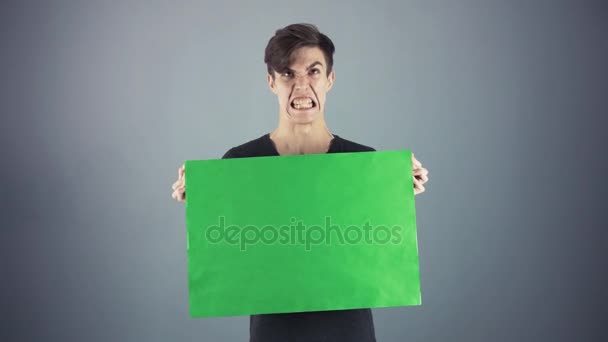 Злой молодой человек в черной рубашке держит зеленый ключ лист плакат серый фон — стоковое видео