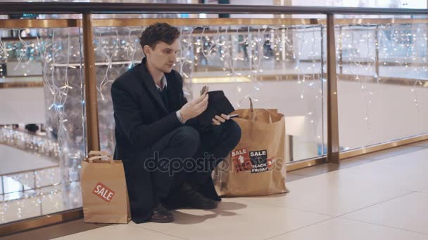 Jeune homme déçu assis sur le sol dans le centre commercial sans argent après les ventes Black Friday — Video