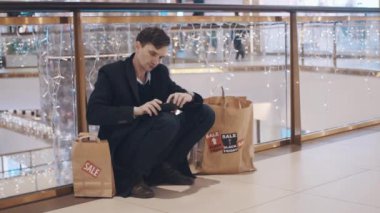 Hayal kırıklığına uğramış genç adam para olmadan alışveriş merkezinde katta oturan Black Friday satış sonrası hizmetler