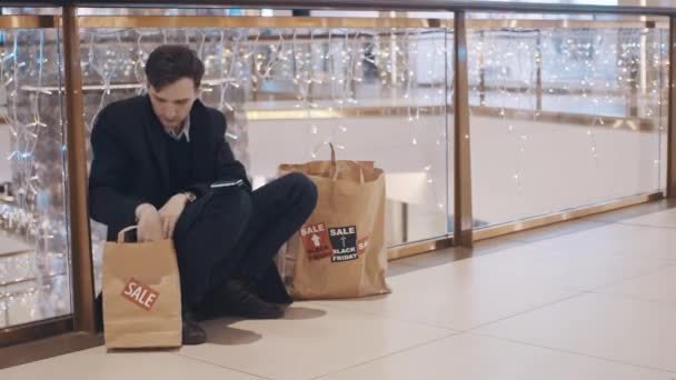 Decepcionado joven sentado en el suelo en el centro comercial sin dinero después de las ventas del Viernes Negro — Vídeo de stock