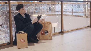Hayal kırıklığına uğramış genç adam para olmadan alışveriş merkezinde katta oturan Black Friday satış sonrası hizmetler