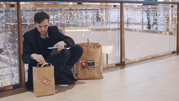 Decepcionado joven sentado en el suelo en el centro comercial sin dinero después de las ventas del Viernes Negro — Vídeos de Stock