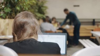 Arka plan üzerinde insanların arkasından kafede dizüstü bilgisayarda çalışan genç iş serbest kadın