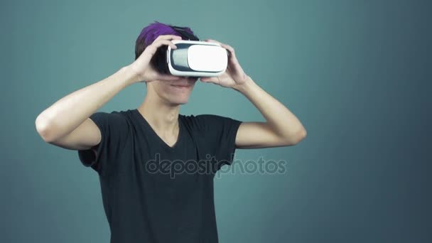 Молодой человек с фиолетовой челкой в наушниках делает жесты, оглядываясь вокруг — стоковое видео