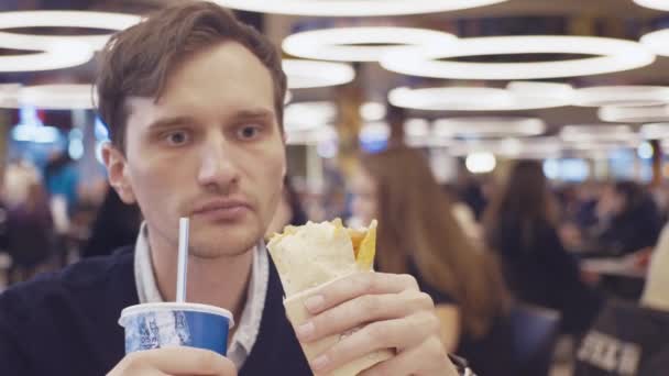 若い男性は、Shawarma ロールを食べるし、ショッピング モールのフードコートでコーラを飲みます。肖像画 — ストック動画