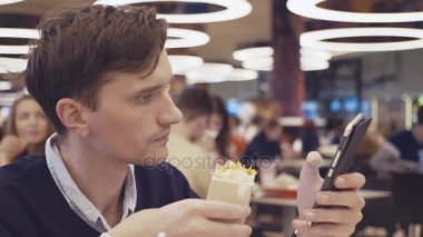 Genç erkekler Smartphone kullanarak Shawarma rulo alışveriş merkezi food court yemek yiyin. Portre