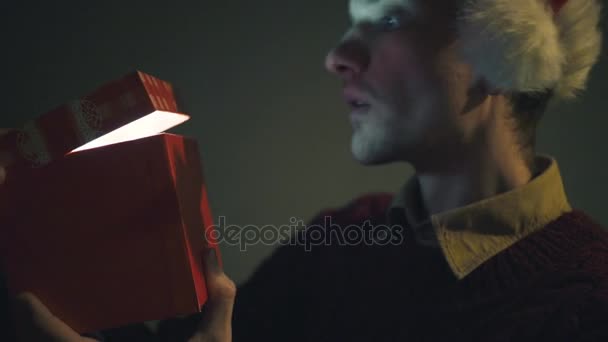 Primer plano del hombre sorprendido abriendo caja de regalo luminosa en la noche Nochebuena — Vídeos de Stock