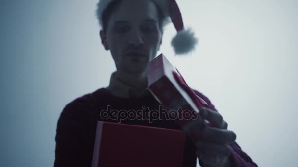 Joven en rojo Santa Claus sombrero openinng caja de regalo sorprendido y feliz con lo que ves — Vídeo de stock