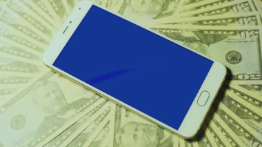 Erkek el ile mavi anahtar göstermek dolar yığını üzerinde beyaz akıllı telefon srceen dokunmadan yakın çekim