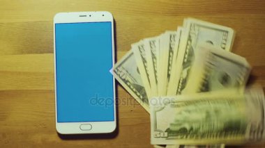 Erkek el banknot yığını üzerinde beyaz akıllı telefon srceen ahşap masa mavi tuş ile atar