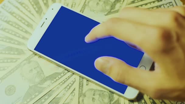 Male hand touching srceen of white smartphone with blue key display on pile of banknote — Stock Video