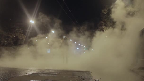 Мужчина идет к камере на ночной улице, покрытой паром от аварии на водосточной трубе — стоковое видео