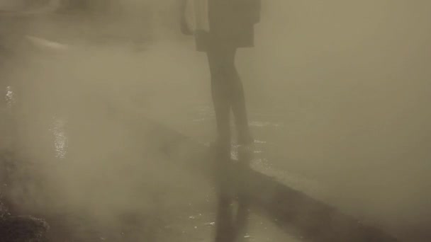 Femme debout sur la frontière d'asphalte au-dessus de l'eau chaude fumante dans la rue de la ville de nuit — Video