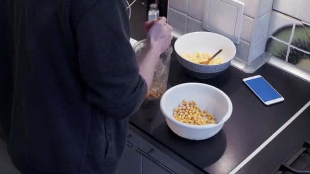 Człowiek, przygotowując pokarm roślinny w domowej kuchni i oglądanie wideo w smartfonie — Wideo stockowe