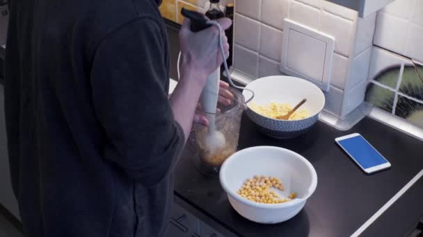 Hombre joven con licuadora cocina desayuno en casa cocina y mira el teléfono inteligente — Vídeo de stock