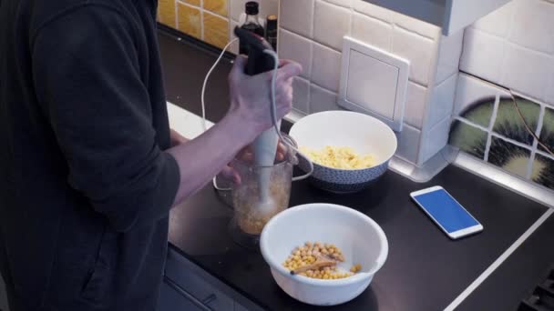 Joven con licuadora cocinando en la cocina casera y viendo video en el teléfono inteligente — Vídeo de stock