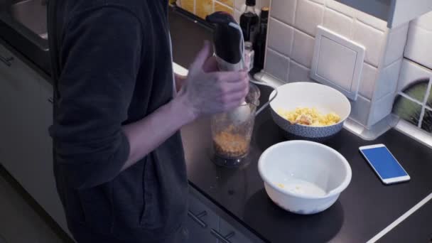 Junger Mann mit Mixer bereitet Gemüse zu und schaut Video am Smartphone — Stockvideo