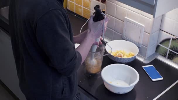 Joven con licuadora preparando comida vegetal en casa cocina y teléfono inteligente — Vídeos de Stock