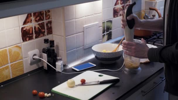 Młody człowiek za pomocą blendera w kuchni i oglądanie wideo w smartfonie — Wideo stockowe