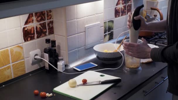 Joven con licuadora preparando comida vegetal en casa cocina y teléfono inteligente — Vídeos de Stock