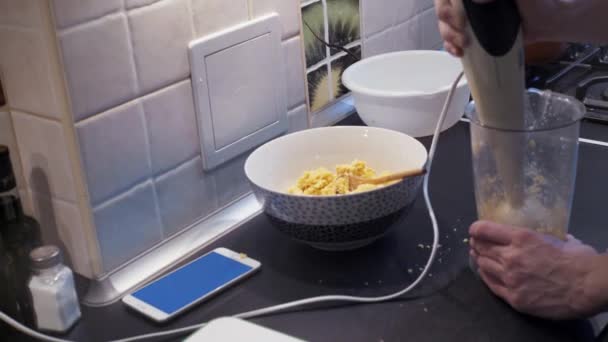 Jovem cozinhar comida vegetariana saudável na cozinha e usando smartphone — Vídeo de Stock