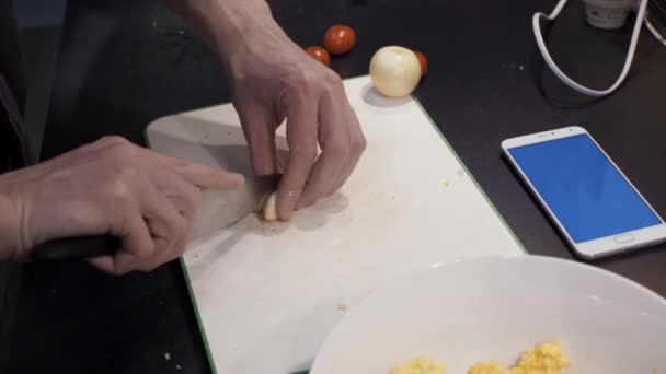 Hands of young man cutting garlic at home kitchen. Chroma key smartphone — Stock Video