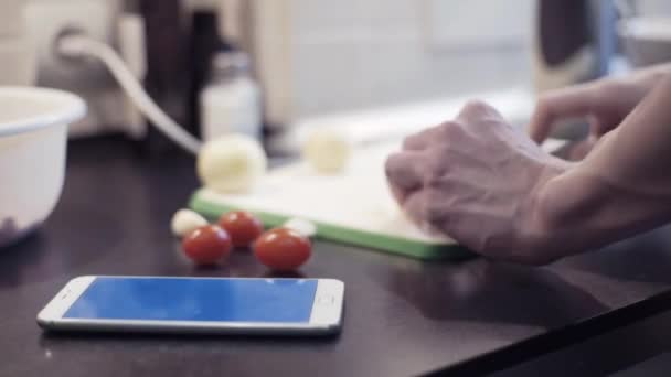 Mains homme coupant l'oignon à la cuisine préparant des aliments végétaux et en utilisant smartphone — Video