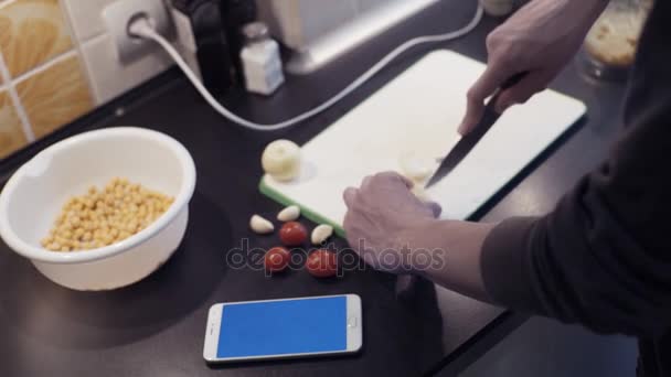 Male hands cut garlic at kitchen preparing vegetable food and using smartphone — Stock Video