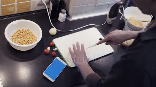 Hands of man cutting garlic at home kitchen and watching video at smartphone — Stock Video