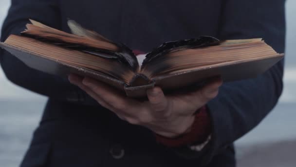 Ung man med brinnande bok i handen stående på kusten storm moln på bakgrund — Stockvideo