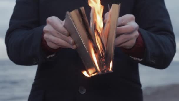 Giovane uomo con libro in fiamme in mano in piedi sulla costa nuvole tempesta sullo sfondo — Video Stock