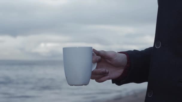 Joven con la taza ardiendo en la mano de pie en la costa nubes de tormenta en el fondo — Vídeos de Stock