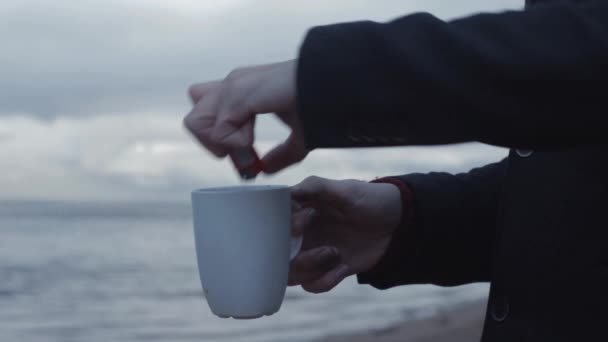 年轻人与燃烧的杯子在手站立在海岸风暴云彩在背景 — 图库视频影像