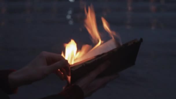 Giovane uomo lettura libro in fiamme in piedi sulla costa nuvole tempesta sullo sfondo — Video Stock