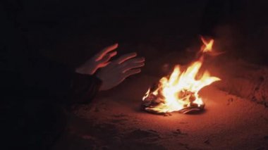 Kum sahilinde üzerinde yanan ayakkabı şenlik ateşi yakın oturma genç adamın elini